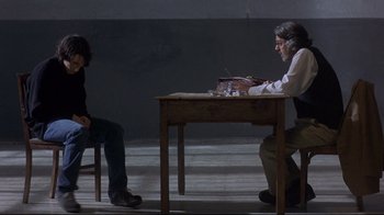 Movie still from “Open Your Eyes” (1997), directed by Alejandro Amenábar – Two people sitting at a table in a dark room; Wide shot, Over the shoulder angle