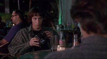 Movie still from “Open Your Eyes” (1997), directed by Alejandro Amenábar – A man sitting in front of a table holding a cell phone; Medium shot, Over the shoulder angle