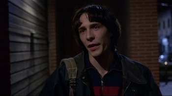 Movie still from “Open Your Eyes” (1997), directed by Alejandro Amenábar – A young man with a backpack standing in front of a brick wall; Close Up shot, Over the shoulder angle