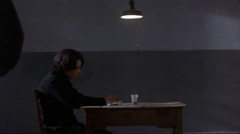 Movie still from “Open Your Eyes” (1997), directed by Alejandro Amenábar – A man sitting at a table with a glass of water; Medium shot, Over the shoulder angle