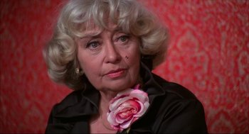 Movie still from “Opening Night” (1977), directed by John Cassavetes – An older woman wearing a black shirt with a pink flower in her neck; Close Up shot, High angle