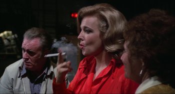 Movie still from “Opening Night” (1977), directed by John Cassavetes – A woman smoking a cigarette in front of two other people; Medium shot, Over the shoulder angle