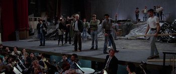Movie still from “Opera” (1987), directed by Dario Argento – A group of people standing on a stage with instruments; Wide shot, High angle