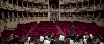 Movie still from “Opera” (1987), directed by Dario Argento – A man standing in front of an orchestra in an auditorium; Extreme Wide shot, High angle