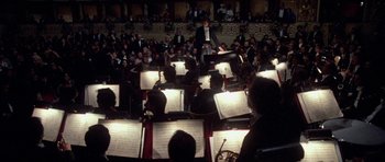 Movie still from “Opera” (1987), directed by Dario Argento – A group of people sitting in front of a microphone; Wide shot, High angle