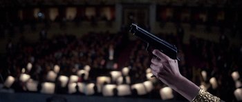 Movie still from “Opera” (1987), directed by Dario Argento – A person holding a gun in front of an audience; Close Up shot, Low angle