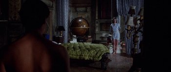 Movie still from “Opera” (1987), directed by Dario Argento – A woman standing next to a bed in a room; Wide shot, High angle