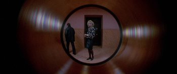 Movie still from “Opera” (1987), directed by Dario Argento – A man and a woman standing in front of an open door; Wide shot, High angle