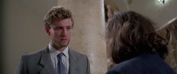 Movie still from “Opera” (1987), directed by Dario Argento – A man wearing a suit and tie talking to a woman; Close Up shot, Over the shoulder angle