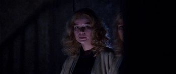 Movie still from “Opera” (1987), directed by Dario Argento – A woman with blonde curly hair standing in a dark room; Close Up shot, Low angle