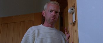 Movie still from “Opera” (1987), directed by Dario Argento – A man in a white sweater standing in front of a toilet paper roll; Close Up shot, Low angle