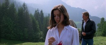 Movie still from “Opera” (1987), directed by Dario Argento – A young woman holding a knife with blood on it in front of trees; Medium shot, High angle