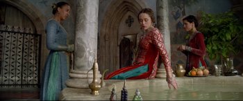 Movie still from “Ophelia” (2018), directed by Claire McCarthy – A woman in a red and blue dress sitting on a table; Wide shot, High angle