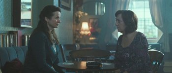 Movie still from “Oranges and Sunshine” (2010), directed by Jim Loach – Two people sitting at a table in front of a lamp; Medium shot, Over the shoulder angle