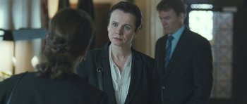 Movie still from “Oranges and Sunshine” (2010), directed by Jim Loach – A woman wearing a suit and tie standing next to two other people; Close Up shot, Over the shoulder angle