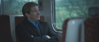 Movie still from “Oranges and Sunshine” (2010), directed by Jim Loach – A man in a suit sitting on a train looking out the window; Medium shot, Over the shoulder angle