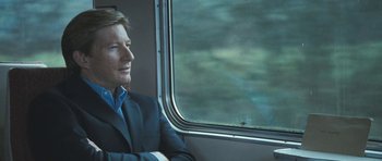 Movie still from “Oranges and Sunshine” (2010), directed by Jim Loach – A man in a suit sitting on a train looking out the window; Close Up shot, Over the shoulder angle