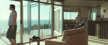 Movie still from “Oranges and Sunshine” (2010), directed by Jim Loach – A living room with large windows overlooking the ocean; Wide shot, Low angle