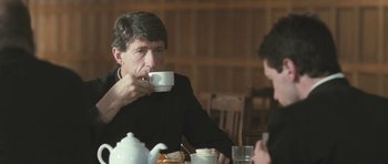 Movie still from “Oranges and Sunshine” (2010), directed by Jim Loach – A man sitting at a table with a cup of tea; Medium shot, Over the shoulder angle