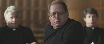 Movie still from “Oranges and Sunshine” (2010), directed by Jim Loach – An older man wearing glasses and a priest's outfit; Close Up shot, Low angle
