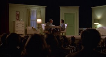 Movie still from “Ordinary People” (1980), directed by Robert Redford – Two people sitting at a table in front of an audience; Wide shot, High angle