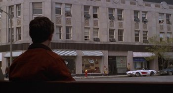 Movie still from “Ordinary People” (1980), directed by Robert Redford – A man sitting in front of a building on a city street; Wide shot, Over the shoulder angle