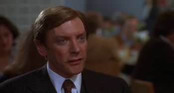 Movie still from “Ordinary People” (1980), directed by Robert Redford – A man in a suit and tie in front of a group of people; Close Up shot, Over the shoulder angle
