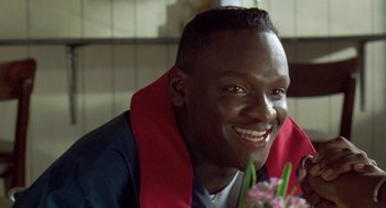 Movie still from “Original Gangstas” (1996), directed by Larry Cohen – A man smiles while sitting in front of flowers; Close Up shot, High angle