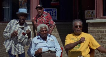 Movie still from “Original Gangstas” (1996), directed by Larry Cohen – A group of men sitting next to each other on a sidewalk; Medium shot, Low angle