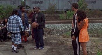Movie still from “Original Gangstas” (1996), directed by Larry Cohen – A group of men standing around a basketball court; Wide shot, Over the shoulder angle