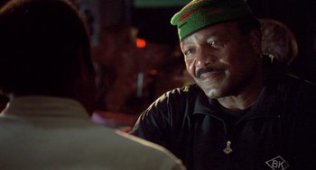 Movie still from “Original Gangstas” (1996), directed by Larry Cohen – An older man wearing a green hat is sitting at a table; Close Up shot, Over the shoulder angle