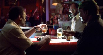 Movie still from “Original Gangstas” (1996), directed by Larry Cohen – Two people sitting at a bar with drinks in front of them; Medium shot, Over the shoulder angle