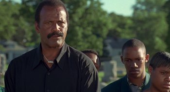 Movie still from “Original Gangstas” (1996), directed by Larry Cohen – A man in a black shirt is standing next to another man; Close Up shot, Low angle