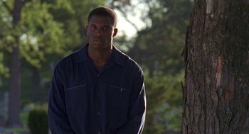 Movie still from “Original Gangstas” (1996), directed by Larry Cohen – A man standing in front of a tree in a park; Medium shot, Low angle