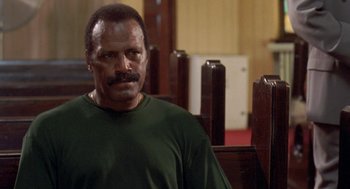 Movie still from “Original Gangstas” (1996), directed by Larry Cohen – A man in a green t - shirt is standing in a room; Close Up shot, Low angle