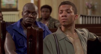 Movie still from “Original Gangstas” (1996), directed by Larry Cohen – Two men in a courtroom looking at a cell phone; Medium shot, Over the shoulder angle