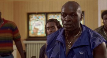 Movie still from “Original Gangstas” (1996), directed by Larry Cohen – A man in a blue shirt is standing next to another man in a blue shirt; Close Up shot, Low angle