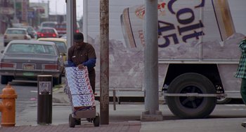 Movie still from “Original Gangstas” (1996), directed by Larry Cohen – A man pushing a cart full of boxes on the side of the street; Wide shot, High angle