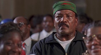 Movie still from “Original Gangstas” (1996), directed by Larry Cohen – An older man wearing a green hat in front of a group of people; Close Up shot, Low angle