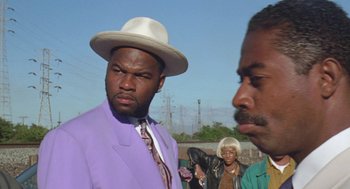 Movie still from “Original Gangstas” (1996), directed by Larry Cohen – A man wearing a purple suit and a white hat; Close Up shot, Over the shoulder angle