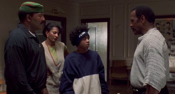 Movie still from “Original Gangstas” (1996), directed by Larry Cohen – A group of people standing in a living room; Medium shot, Over the shoulder angle