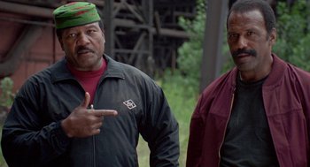 Movie still from “Original Gangstas” (1996), directed by Larry Cohen – Two men standing next to each other on a field; Medium shot, Low angle