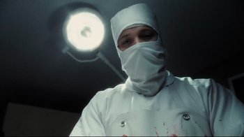 Movie still from “Orphan” (2009), directed by Jaume Collet-Serra – A man wearing a surgical gown and a surgical mask; Close Up shot, Low angle