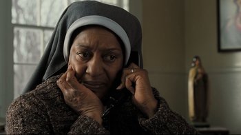 Movie still from “Orphan” (2009), directed by Jaume Collet-Serra – An older woman wearing a headscarf is talking on a cell phone; Close Up shot, Low angle