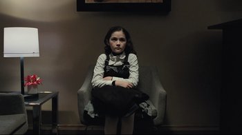 Movie still from “Orphan” (2009), directed by Jaume Collet-Serra – A girl sitting in a chair with her arms crossed; Medium shot, Over the shoulder angle