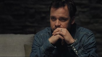 Movie still from “Orphan” (2009), directed by Jaume Collet-Serra – A person sitting on a couch with his hands together; Close Up shot, High angle