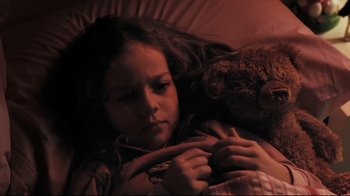 Movie still from “Orphan” (2009), directed by Jaume Collet-Serra – A young girl laying in bed with a teddy bear; Close Up shot, High angle