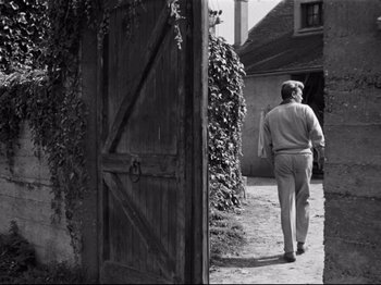 Movie still from “Orpheus” (1950), directed by Jean Cocteau – A black and white photo of a man walking through a doorway; Wide shot, Over the shoulder angle