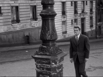 Movie still from “Orpheus” (1950), directed by Jean Cocteau – A black and white photo of a man standing next to a street light; Wide shot, High angle