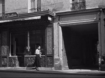 Movie still from “Orpheus” (1950), directed by Jean Cocteau – A woman walking down the street in front of a building; Wide shot, Low angle